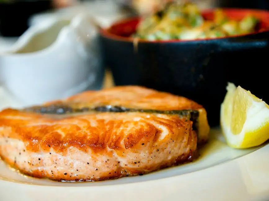 A picture of a fish on a plate beside a lemon. This is what smoked salmon looks like when it is served for a meal.