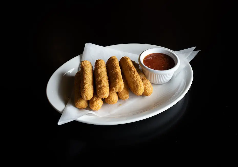A plate of golden, crispy mozzarella sticks with marinara sauce on the side